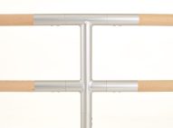 Ballet Barre Extender Product Image Close-up detail shot of a silver metal T-shaped extender joint connecting wooden ballet barre rails.