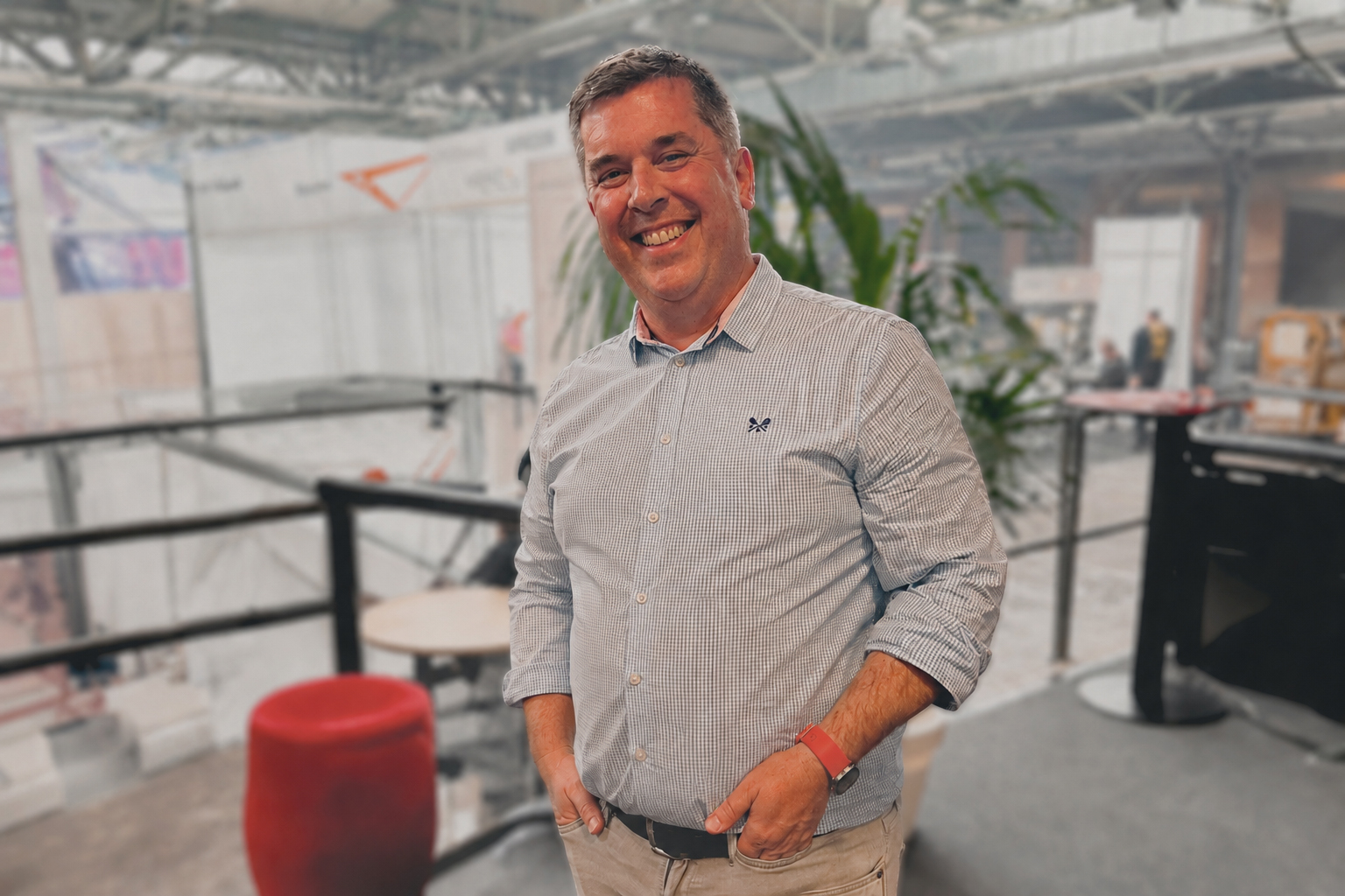 Smiling man in a light blue striped button-down shirt standing in a modern event space.